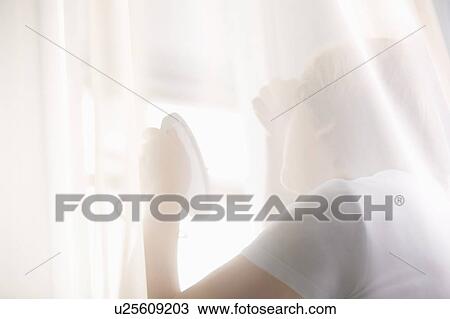 Stock Image - Mature woman looks at reflection in hand mirror. Fotosearch