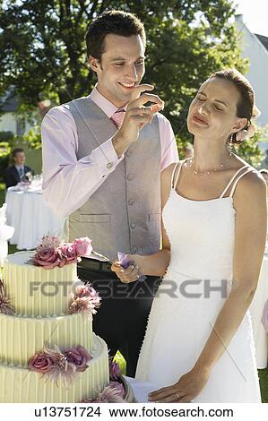 Mid adult bride and groom cutting wedding cake, groom putting bit of cake on bride's nose View Large Photo Image Picture - Mid adult bride and groom cutting wedding cake, groom putting bit of cake on bride's nose. Fotosearch