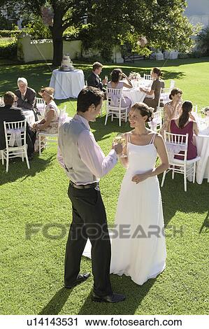 Mid adult bride and groom in garden, toasting among wedding guests View Large Photo Image Stock Image - Mid adult bride and groom in garden, toasting among wedding guests. Fotosearch