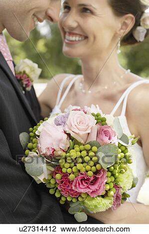 Stock Image - Mid adult bride and groom in garden, smiling, close-up. Fotosearch