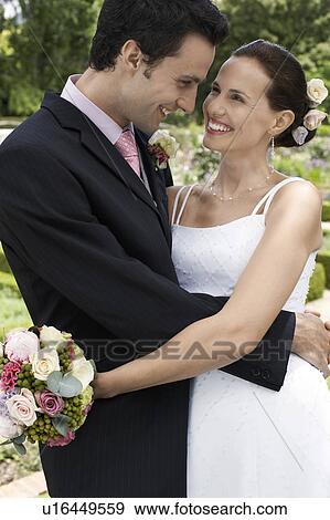 Stock Photo - Mid adult bride and groom in garden, embracing. Fotosearch