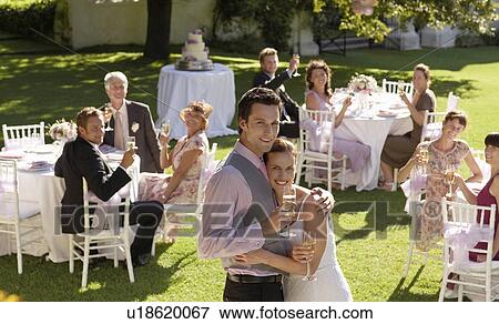 Mid adult bride and groom in garden among wedding guests, holding wineglasses, embracing View Large Photo Image Stock Photo - Mid adult bride and groom in garden among wedding guests, holding wineglasses, embracing. Fotosearch