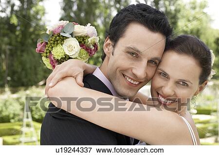 Stock Photo - Mid adult bride and groom in garden, embracing. Fotosearch
