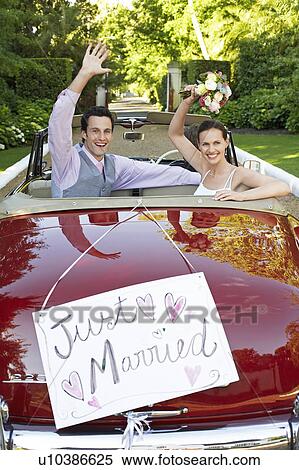 Stock Photography - Mid adult bride and groom in retro car, waving hands. Fotosearch