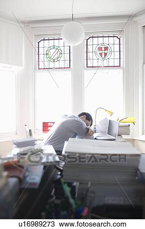 Stock Image - mid adult man sleeps at his desk. Fotosearch