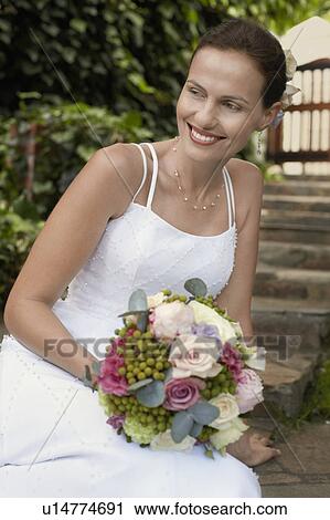 Mid adult woman wearing white dress, holding bouquet, smiling View Large Photo Image Stock Image - Mid adult woman wearing white dress, holding bouquet, smiling. Fotosearch