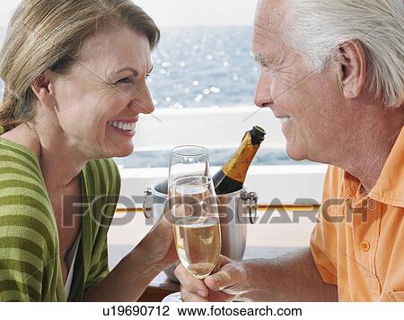 Stock Image - Middle-aged couple drinking champagne on yacht, side view, close-up. Fotosearch