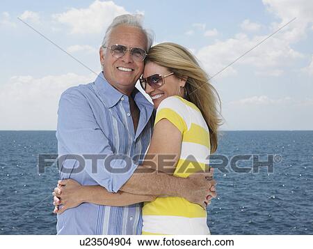 Picture - Middle-aged couple embracing against sea, portrait. Fotosearch