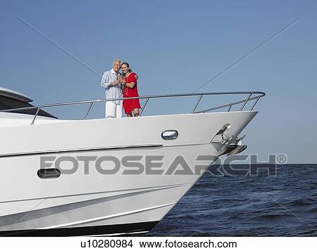 Picture - Middle-aged couple standing in bow of yacht. Fotosearch