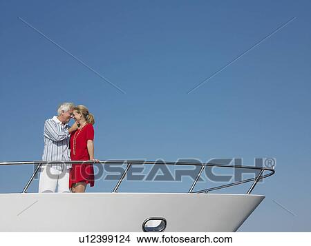 Picture - Middle-aged couple standing in bow of yacht. Fotosearch
