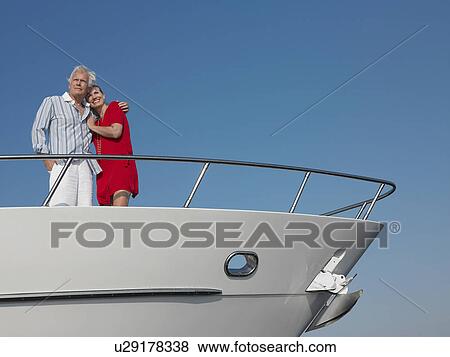 Stock Photo - Middle-aged couple standing in bow of yacht. Fotosearch
