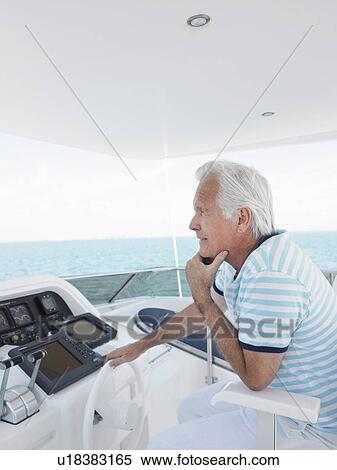 Stock Photography - Middle-aged man sitting at helm of yacht, side view. Fotosearch