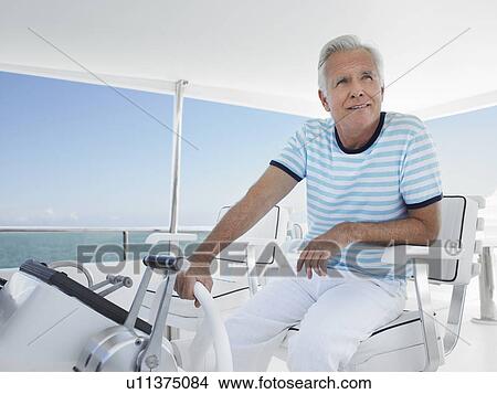 Picture - Middle-aged man sitting at helm of yacht. Fotosearch