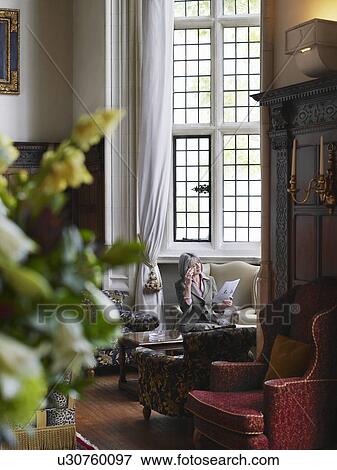 Stock Photo - Middle-aged woman sitting and reading in interior with antique furniture. Fotosearch
