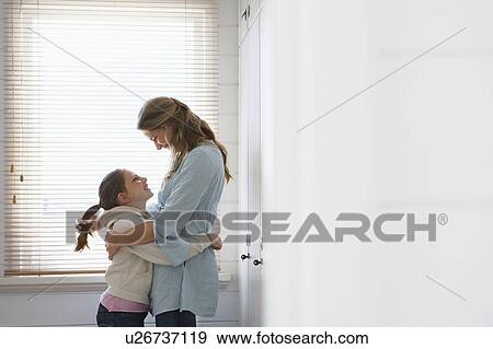 Mother and daughter embracing standing in front of window View Large Photo Image Stock Photo - Mother and daughter embracing standing in front of window. Fotosearch
