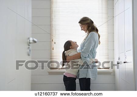 Stock Photo - Mother and daughter hugging, standing in front of window. Fotosearch
