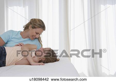Stock Image - Mother and daughter lying on bed, half length. Fotosearch