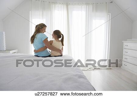 Stock Photo - Mother and daughter sitting on bed in bedroom. Fotosearch