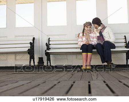 Mother and daughter sitting together on pier bench, low angle view View Large Photo Image Stock Photograph - Mother and daughter sitting together on pier bench, low angle view. Fotosearch