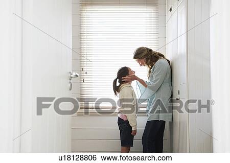 Stock Photograph - Mother cupping daughters face in hands, standing by window. Fotosearch