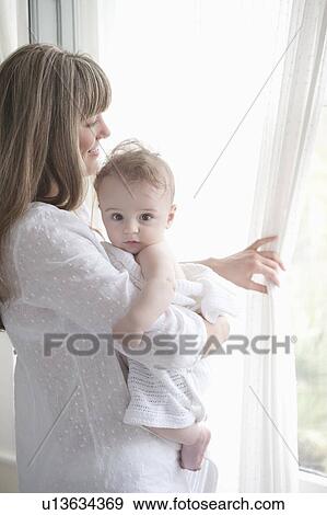Mother stands looking through window while holding a baby boy View Large Photo Image Stock Photo - Mother stands looking through window while holding a baby boy. Fotosearch