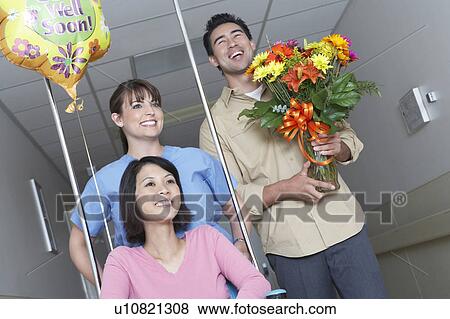 Stock Photo - Nurse and man with bouquet assigning woman on wheelchair in hospital hallway. Fotosearch
