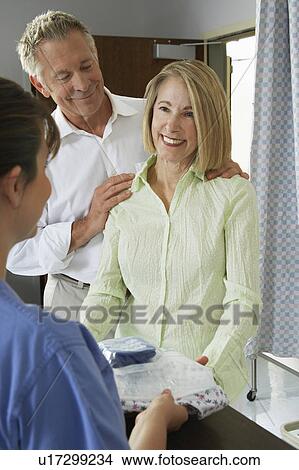 Picture - Nurse giving examination gown to female patient. Fotosearch