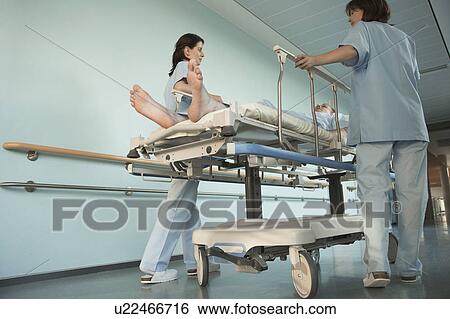 Stock Photograph - Nurses Moving Patient on gurney in hospital Corridor, low angle view. Fotosearch