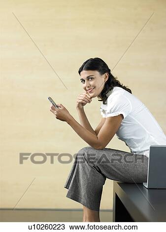 Stock Image - Office worker sitting by laptop sending text message, portrait. Fotosearch