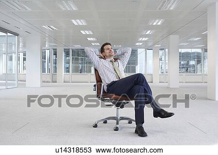 Office worker sitting in swivel chair, hands behind head, in empty office space View Large Photo Image Stock Image - Office worker sitting in swivel chair, hands behind head, in empty office space. Fotosearch