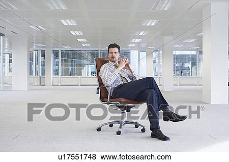 Stock Photo - Office worker sitting in swivel chair, fingertips interlaced, in empty office space. Fotosearch