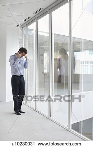 Office worker talking on mobile phone, head down, at window of empty office space View Large Photo Image Stock Image - Office worker talking on mobile phone, head down, at window of empty office space. Fotosearch