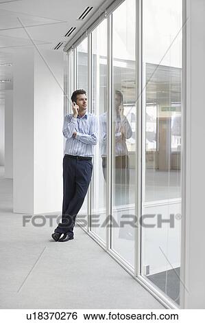 Office worker talking on mobile phone, looking out window in empty office space View Large Photo Image Stock Photograph - Office worker talking on mobile phone, looking out window in empty office space. Fotosearch