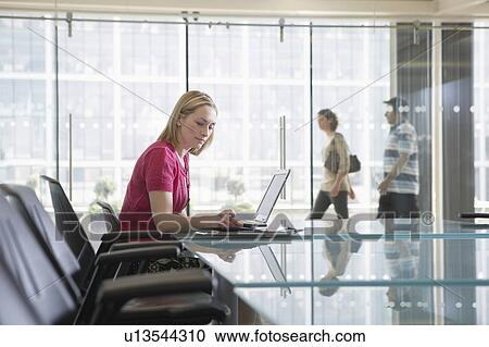 Stock Image - Office worker using laptop, sitting in conference room, side view. Fotosearch