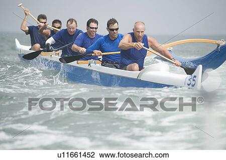 Stock Image - Outrigger canoeing team on water. Fotosearch