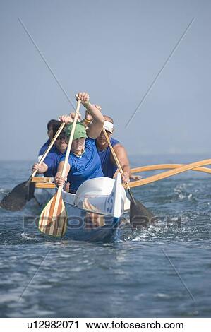 Stock Image - Outrigger canoeing team on water. Fotosearch