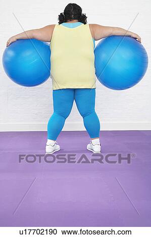 Stock Image - Overweight Woman Holding two Exercise Balls, back view. Fotosearch