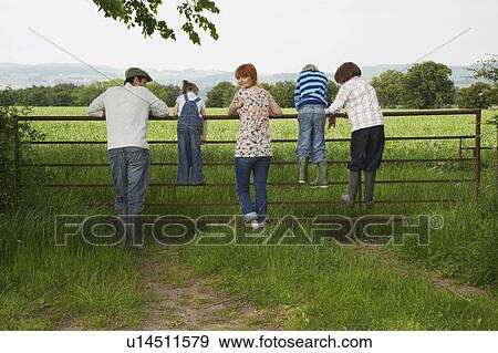 Parents with three children (5-9) standing on fence in countryside View Large Photo Image Stock Photo - Parents with three children (5-9) standing on fence in countryside. Fotosearch