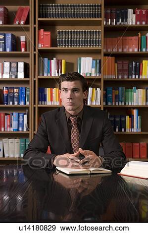 Pensive man wearing suit with book at desk in library View Large Photo Image Stock Photo - Pensive man wearing suit with book at desk in library. Fotosearch