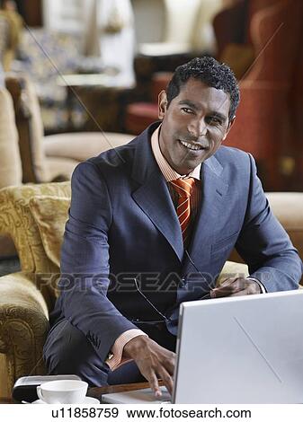 Stock Photo - Portrait of business man sitting in lobby working on laptop, smiling. Fotosearch
