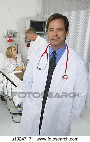 Stock Image - Portrait of doctor in hospital room, patient in background. Fotosearch