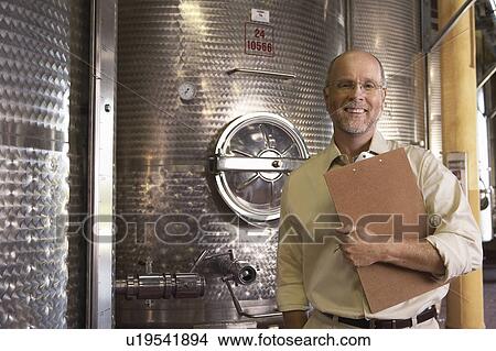 Picture - Portrait of winemaker standing next to wine vat holding clipboard. Fotosearch