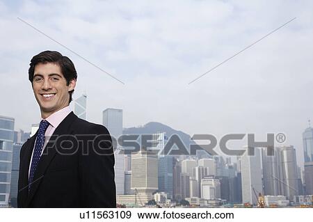 Stock Photo - Portrait of young business man smiling, office buildings in background. Fotosearch