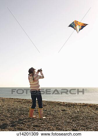 Stock Photo - Pre teen girl flying kite on beach, full length. Fotosearch