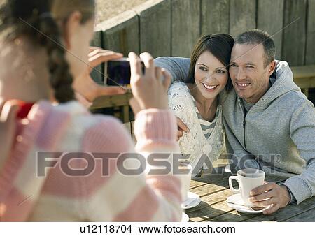 Pre teen girl photographing parents sitting at outdoor table View Large Photo Image Picture - Pre teen girl photographing parents sitting at outdoor table. Fotosearch
