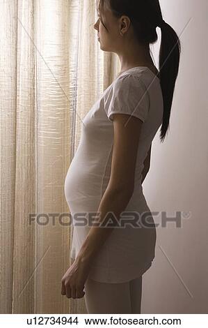 Pregnant woman stands at window with closed curtains View Large Photo Image Picture - Pregnant woman stands at window with closed curtains. Fotosearch