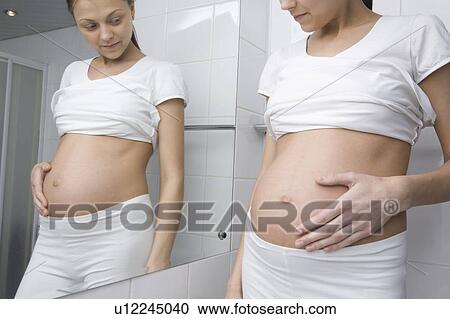 Pregnant woman stands looking at stomach in bathroom mirror View Large Photo Image Stock Image - Pregnant woman stands looking at stomach in bathroom mirror. Fotosearch
