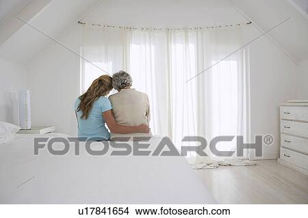 Rear view of adult daughter with her arm around mother in white bedroom View Large Photo Image Picture - Rear view of adult daughter with her arm around mother in white bedroom. Fotosearch