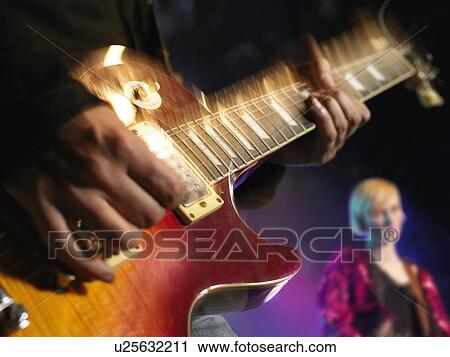Stock Image - Rock Guitarist on stage in Concert, mid-section, close up of guitar. Fotosearch