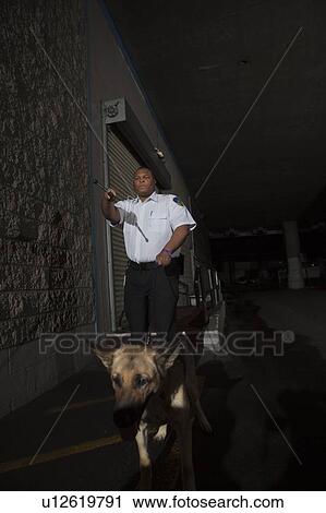 Stock Image - Security guard in alleyway pursuit with guard dog. Fotosearch